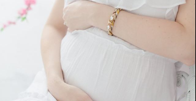 woman-in-soft-white-dress-sits-and-holds-her-pregnant-belly